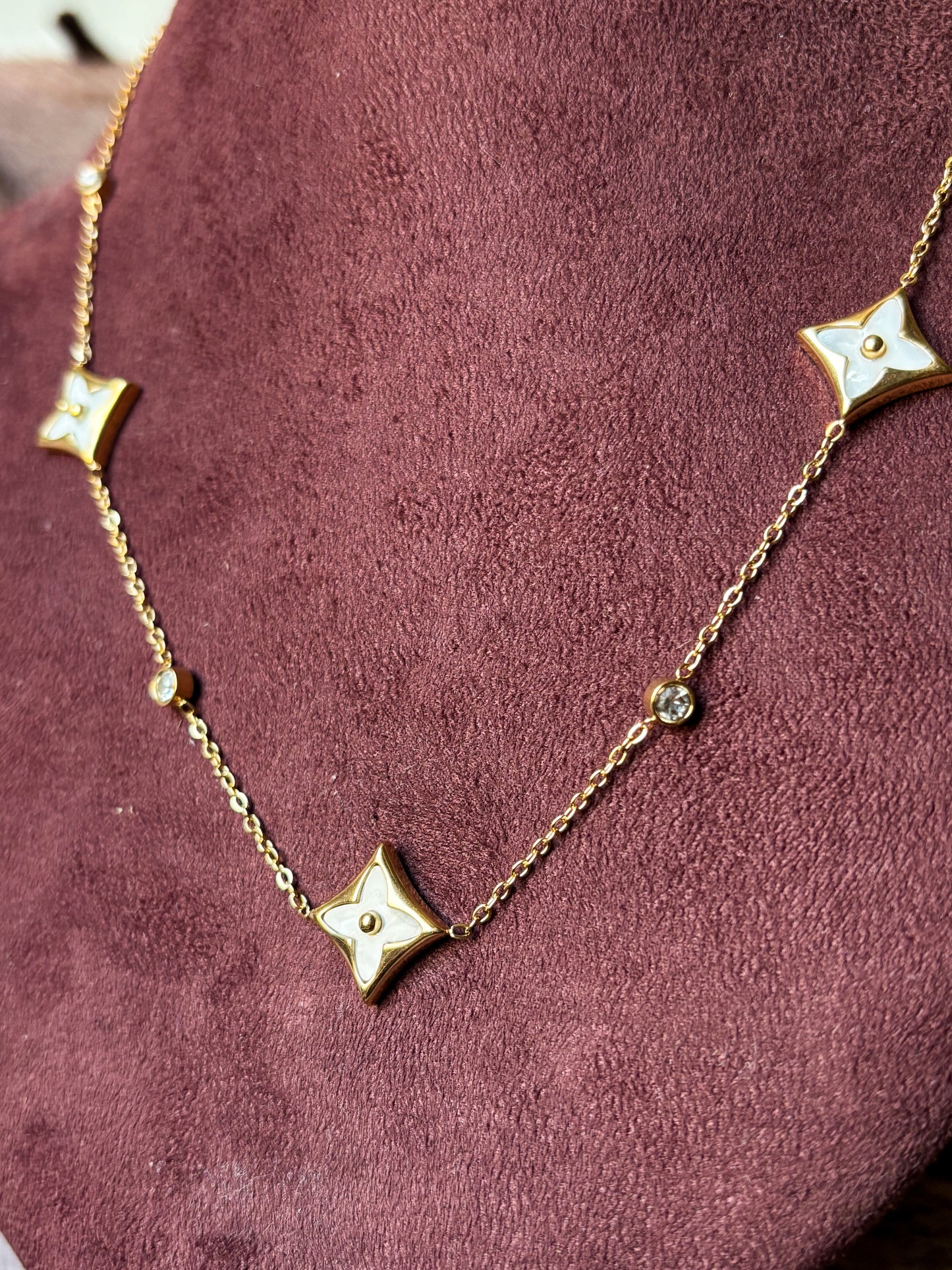 A delicate gold clover charm necklace with sparkling crystal accents, styled with a soft neutral outfit for an elegant everyday jewellery look.