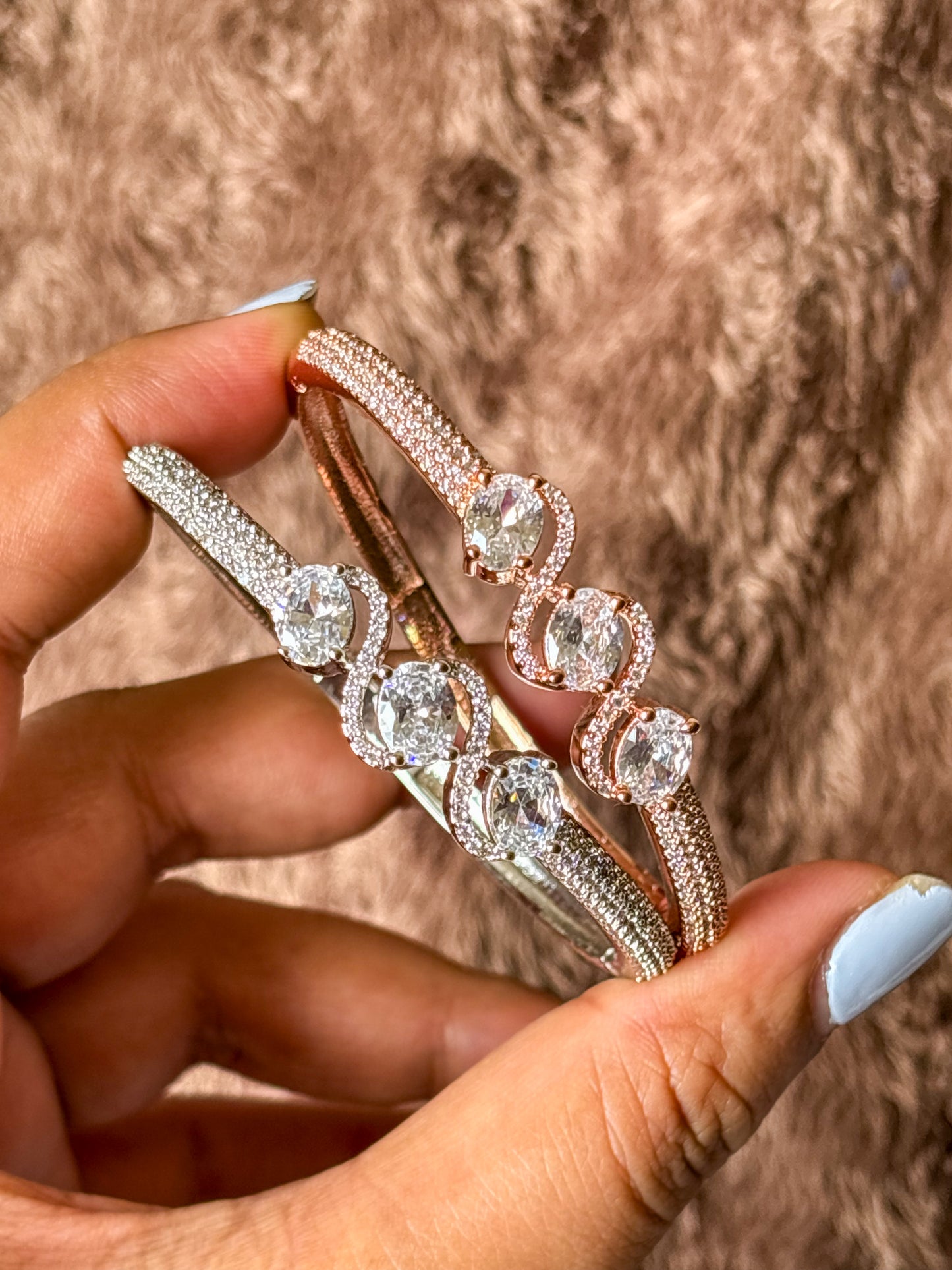 Elegant rose gold & silver AD bracelets with sparkling stones on a smooth wrist, photographed on a soft textured fabric background in warm natural lighting.