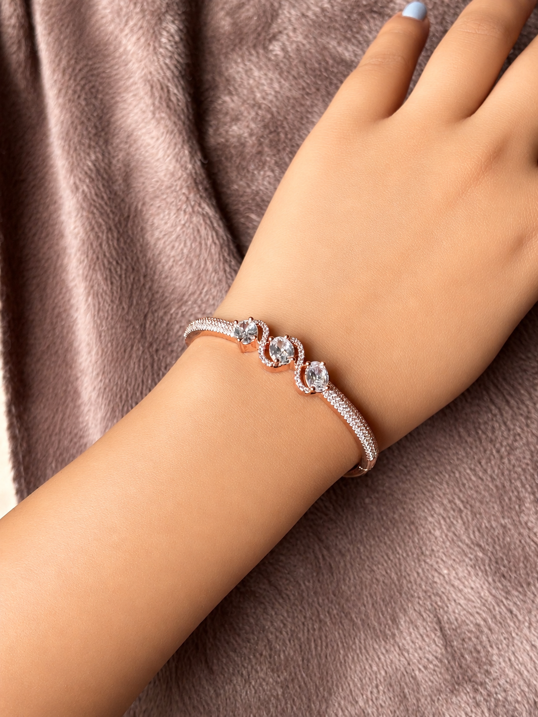 Elegant rose gold & silver AD bracelets with sparkling stones on a smooth wrist, photographed on a soft textured fabric background in warm natural lighting.