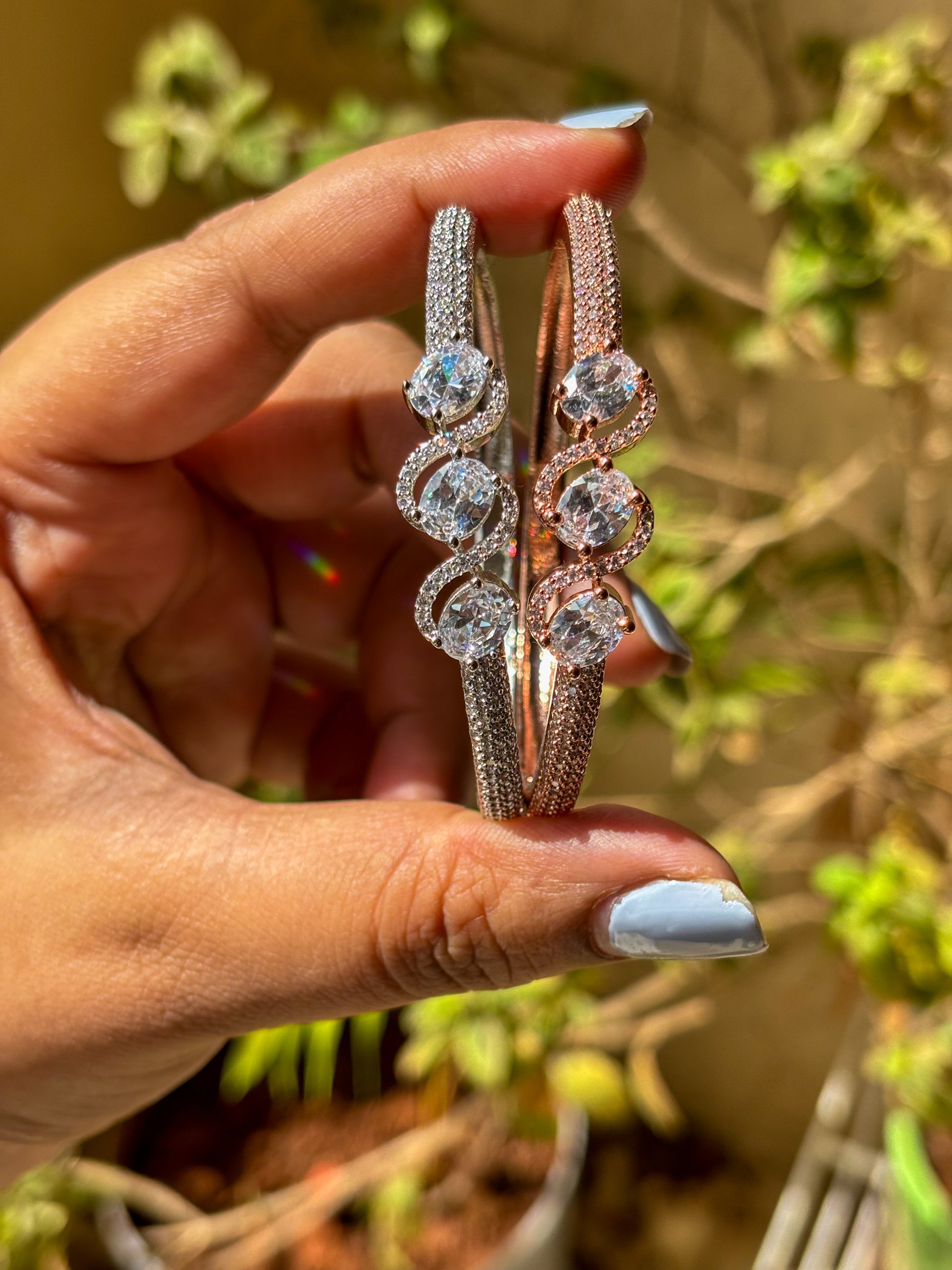 Elegant rose gold & silver AD bracelets with sparkling stones on a smooth wrist, photographed in warm natural lighting.