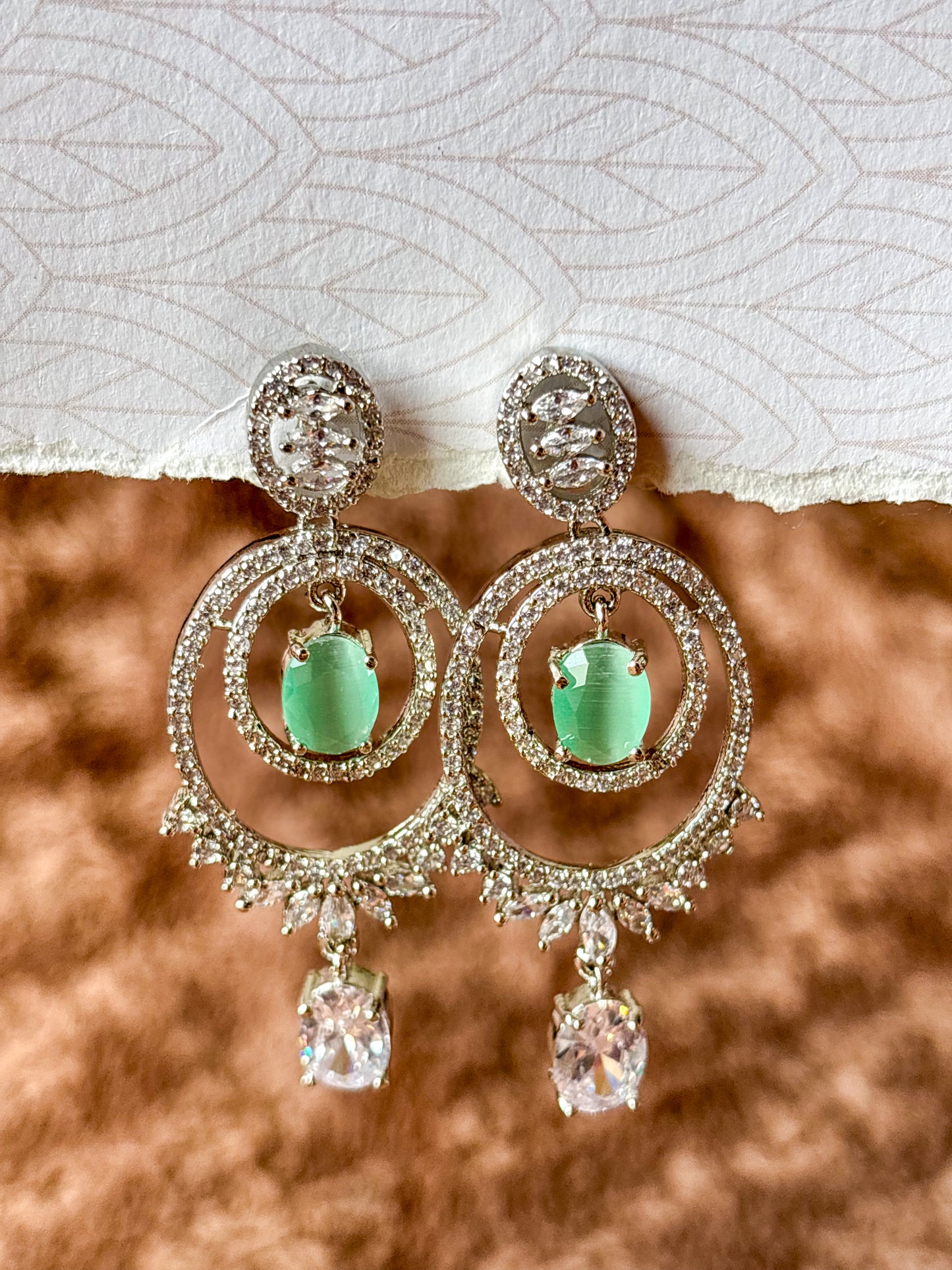 Elegant silver-tone chandelier earrings with emerald green center stones and sparkling zircon detailing.