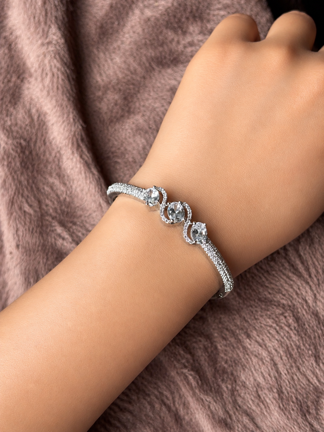 Elegant rose gold & silver AD bracelets with sparkling stones on a smooth wrist, photographed on a soft textured fabric background in warm natural lighting.