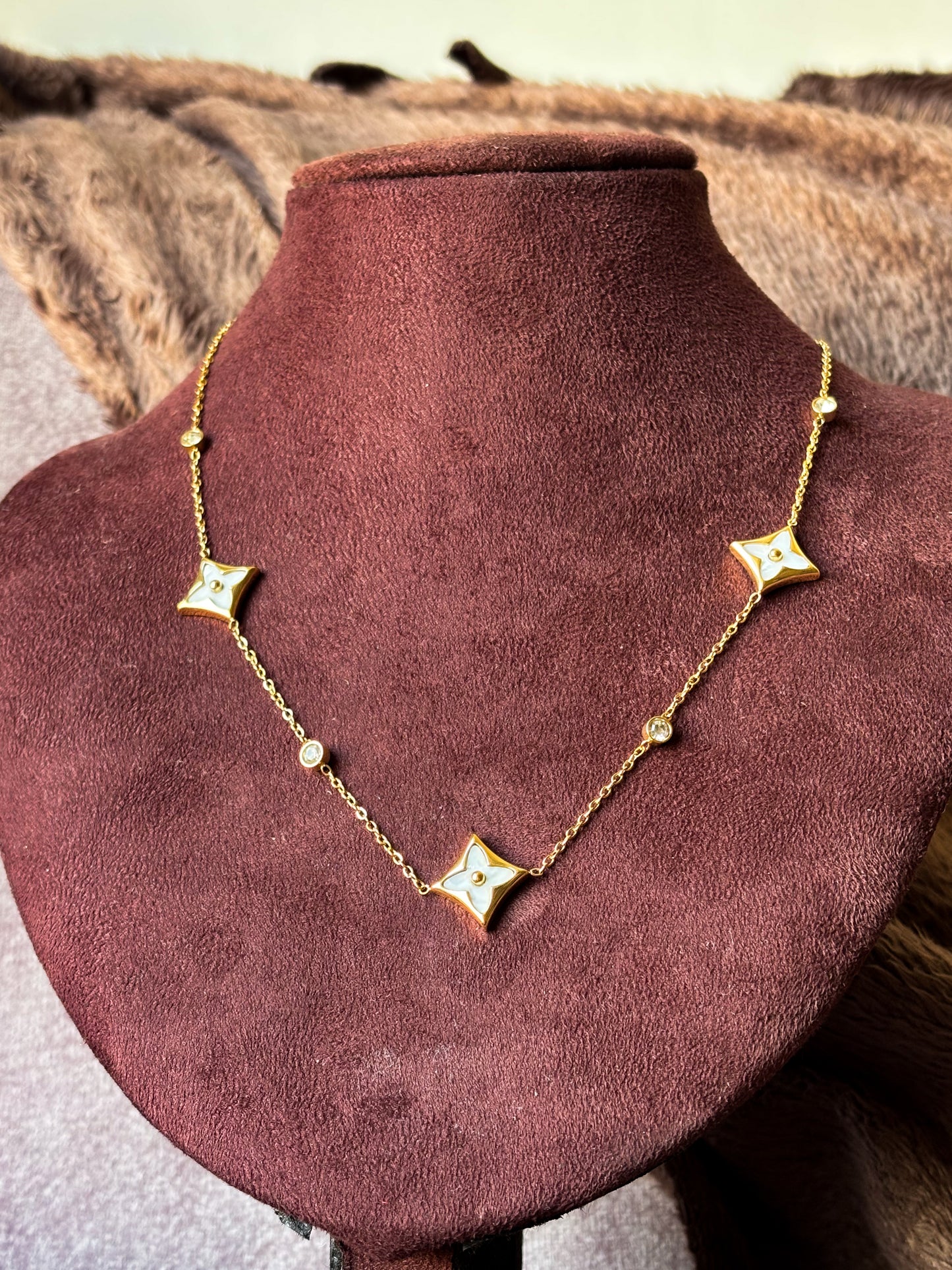 A delicate gold clover charm necklace with sparkling crystal accents, styled with a soft neutral outfit for an elegant everyday jewellery look.