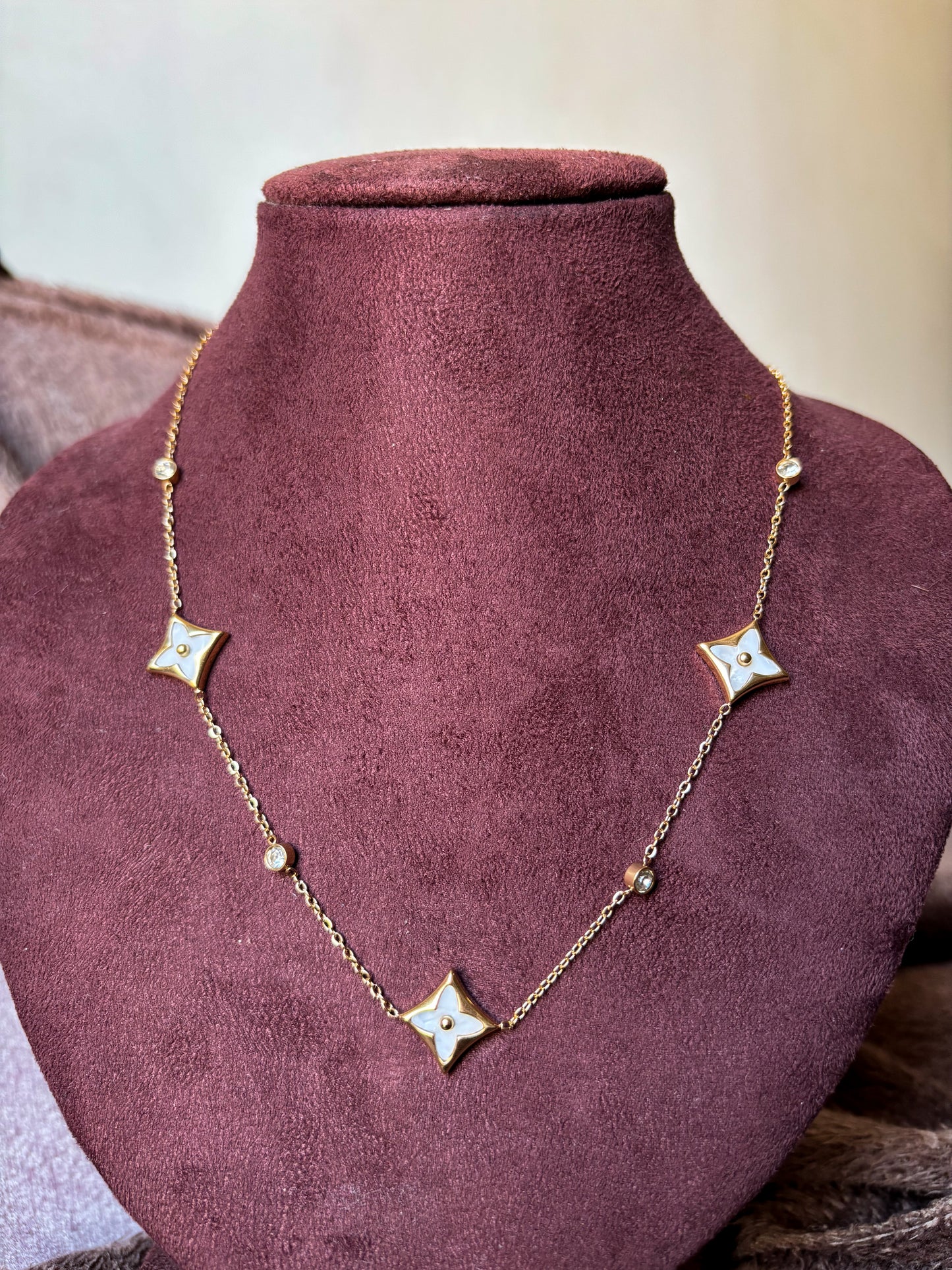 A delicate gold clover charm necklace with sparkling crystal accents, styled with a soft neutral outfit for an elegant everyday jewellery look.