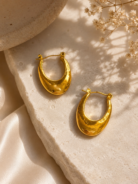 Elegant anti-tarnish gold teardrop hoop earrings with a sleek polished finish, displayed on a soft beige stone and satin aesthetic background. Lightweight, waterproof statement hoops perfect for everyday wear and special occasions.