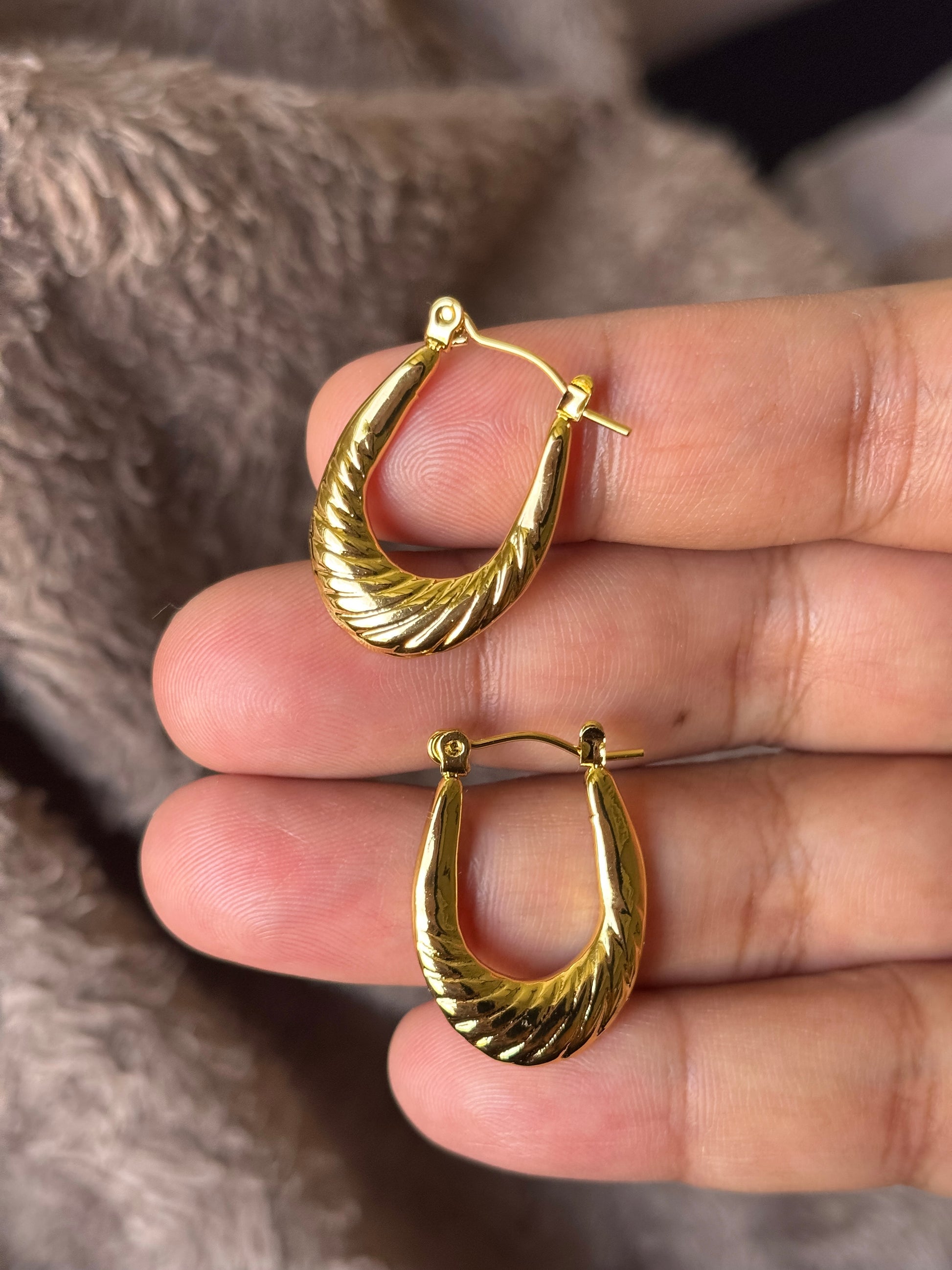 Anti tarnish textured gold hoop earrings with a sculpted twisted design, displayed on a soft neutral aesthetic background. Lightweight waterproof statement hoops with a polished gold finish for everyday wear.
