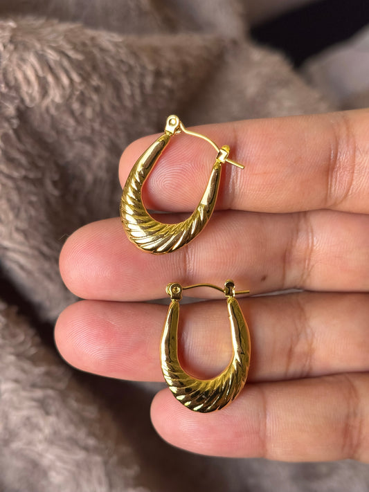 Anti tarnish textured gold hoop earrings with a sculpted twisted design, displayed on a soft neutral aesthetic background. Lightweight waterproof statement hoops with a polished gold finish for everyday wear.