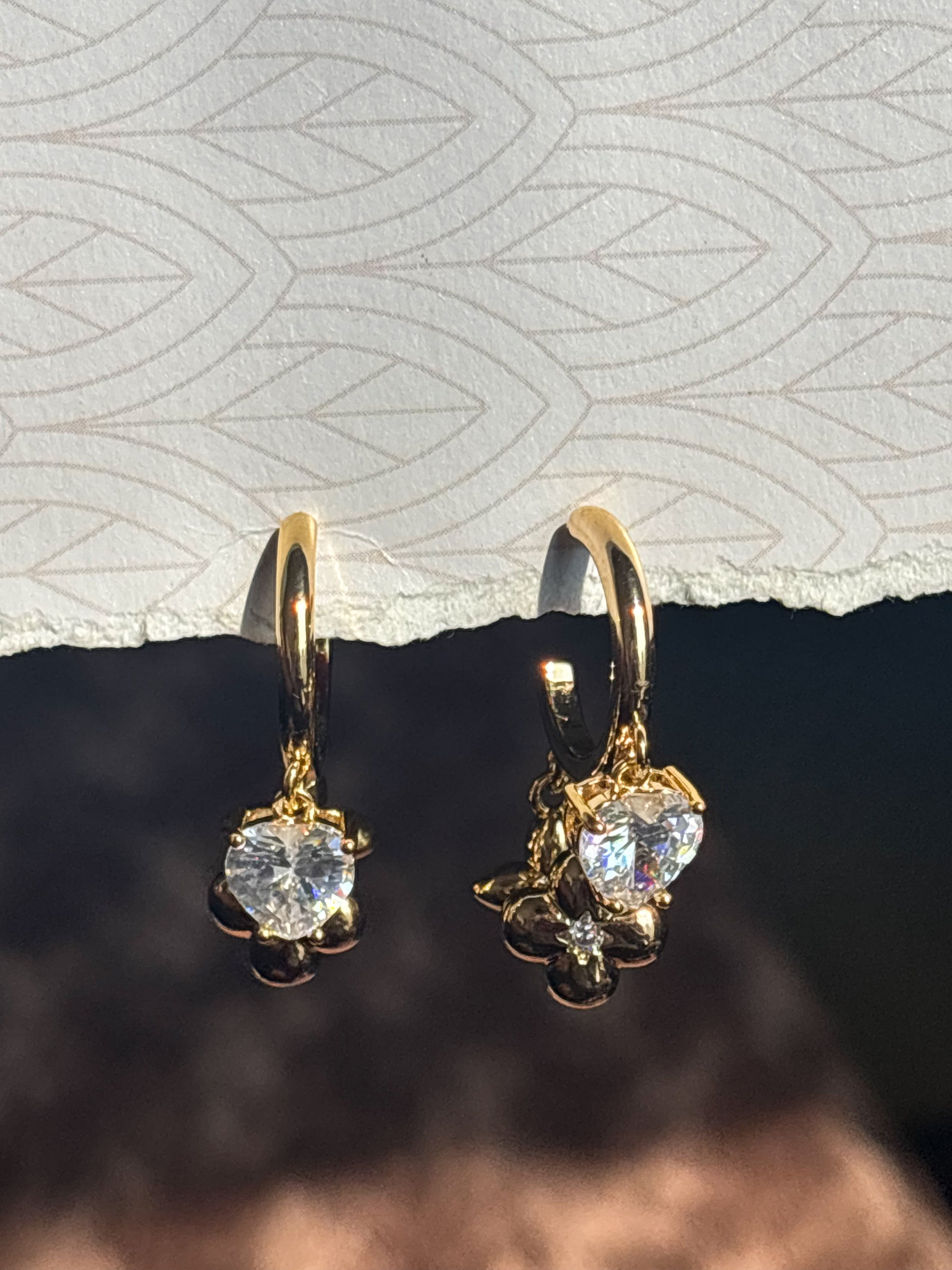 Gold earrings with clear gemstones on a textured surface