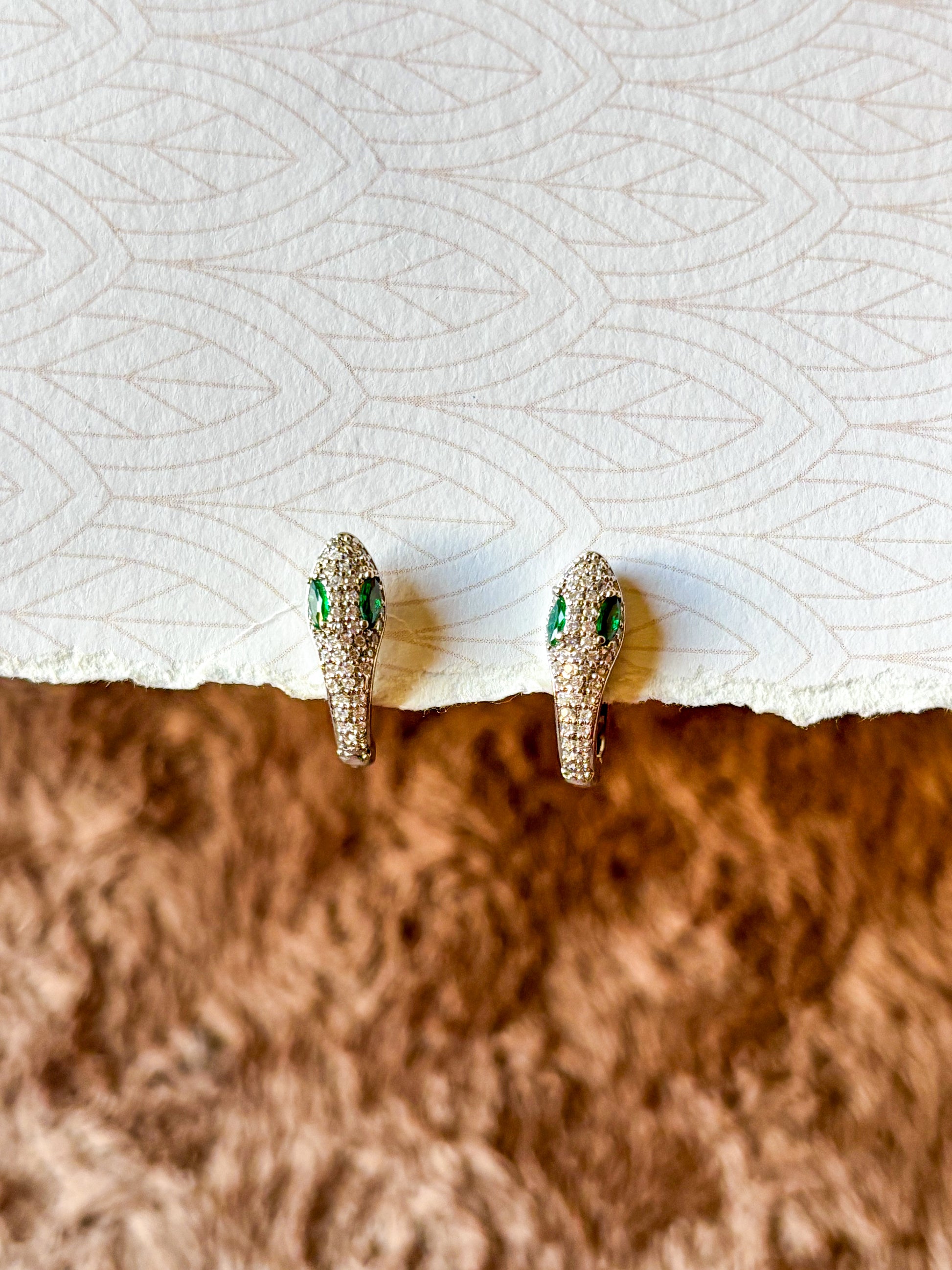 A sparkling emerald serpent hoop earring featuring pavé-set crystals and vibrant green gemstone eyes.