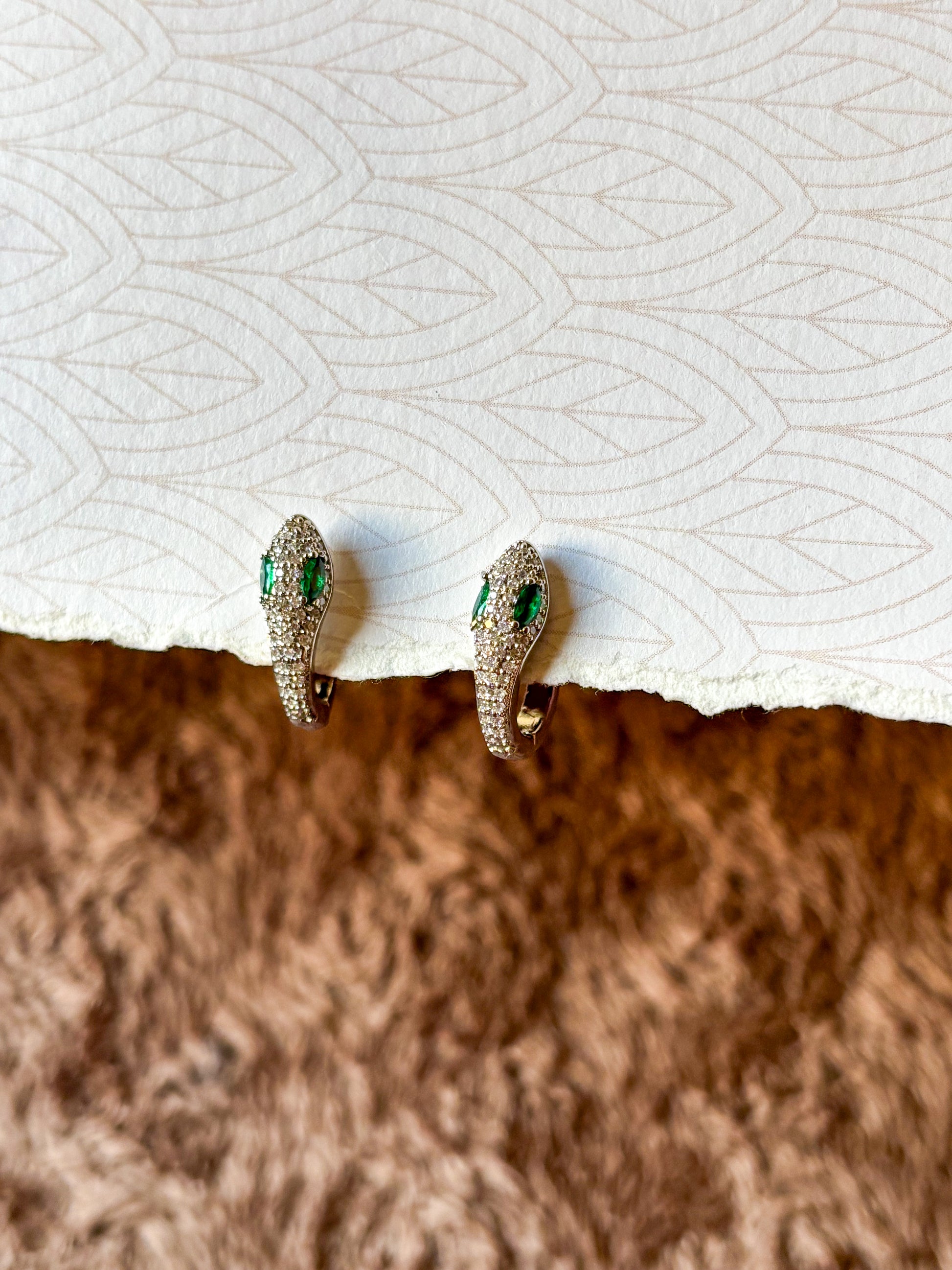 A sparkling emerald serpent hoop earring featuring pavé-set crystals and vibrant green gemstone eyes.