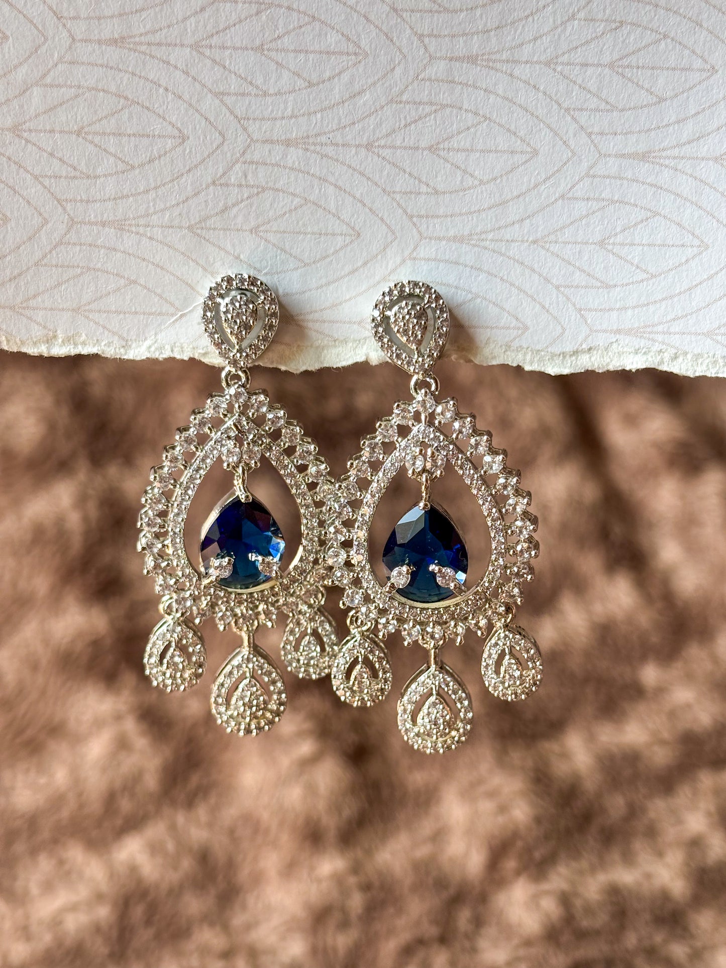 Sparkling silver-tone American Diamond (AD) Chandbali earrings featuring a large teardrop-cut crystal centerpiece, intricate pavé stone detailing and elegant dangling accents. Perfect for bridal wear, weddings, festive occasions and party styling.