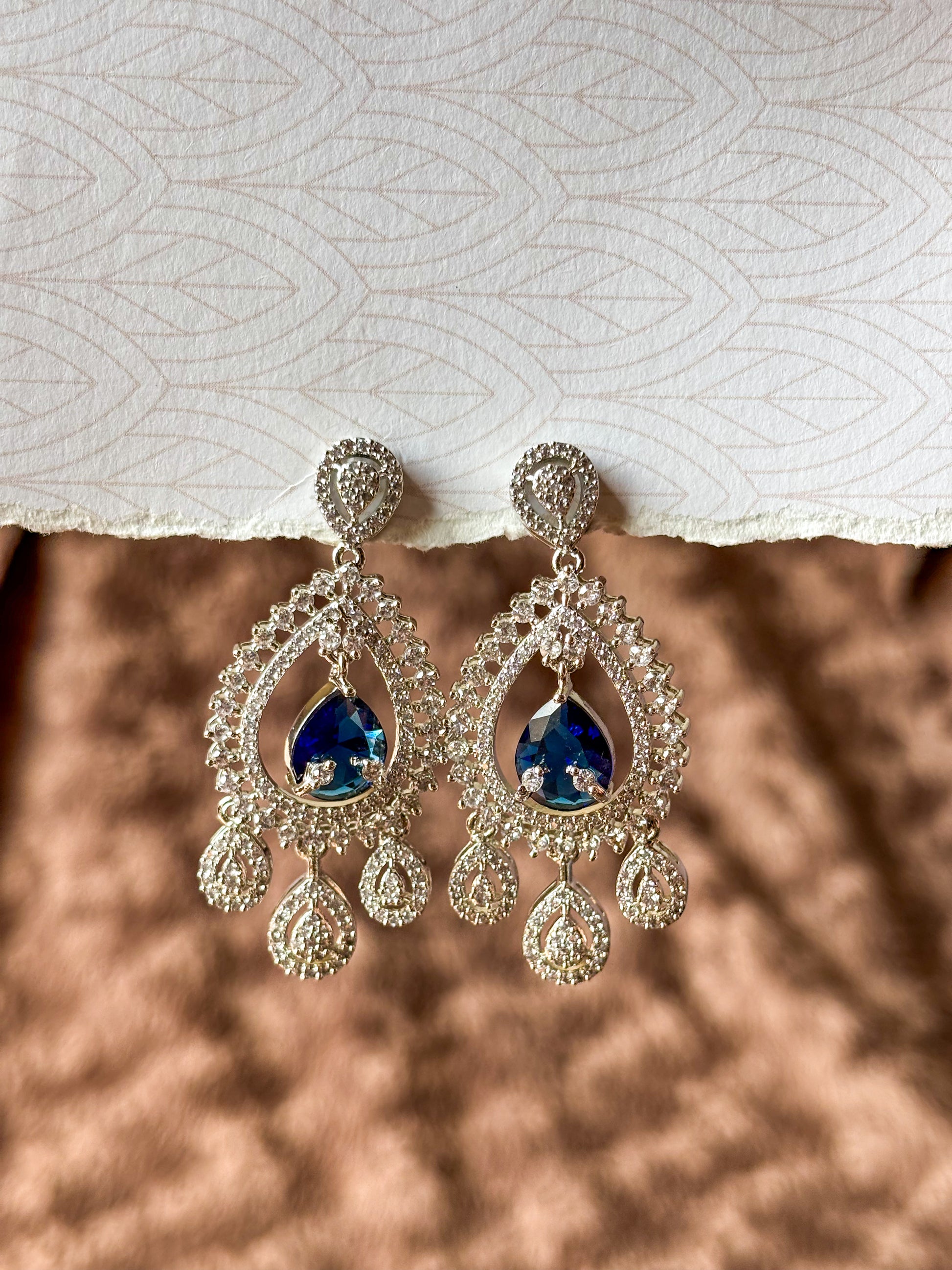 Sparkling silver-tone American Diamond (AD) Chandbali earrings featuring a large teardrop-cut crystal centerpiece, intricate pavé stone detailing and elegant dangling accents. Perfect for bridal wear, weddings, festive occasions and party styling.