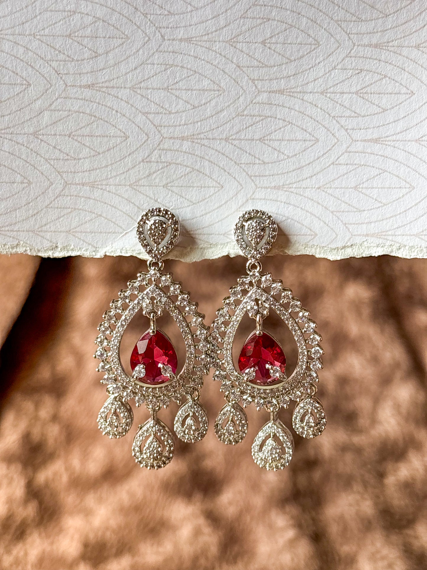 Sparkling silver-tone American Diamond (AD) Chandbali earrings featuring a large teardrop-cut crystal centerpiece, intricate pavé stone detailing and elegant dangling accents. Perfect for bridal wear, weddings, festive occasions and party styling.