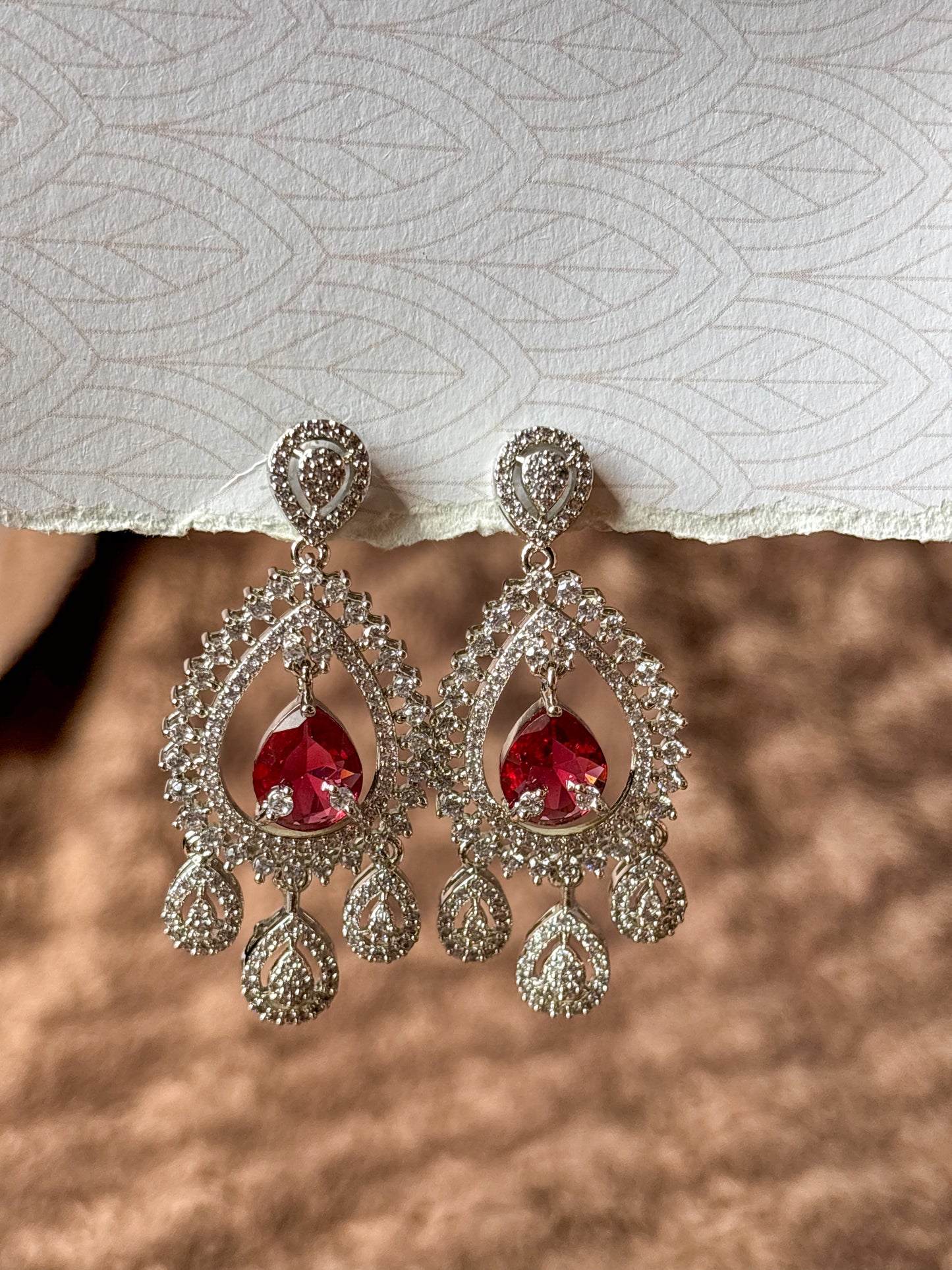 Sparkling silver-tone American Diamond (AD) Chandbali earrings featuring a large teardrop-cut crystal centerpiece, intricate pavé stone detailing and elegant dangling accents. Perfect for bridal wear, weddings, festive occasions and party styling.