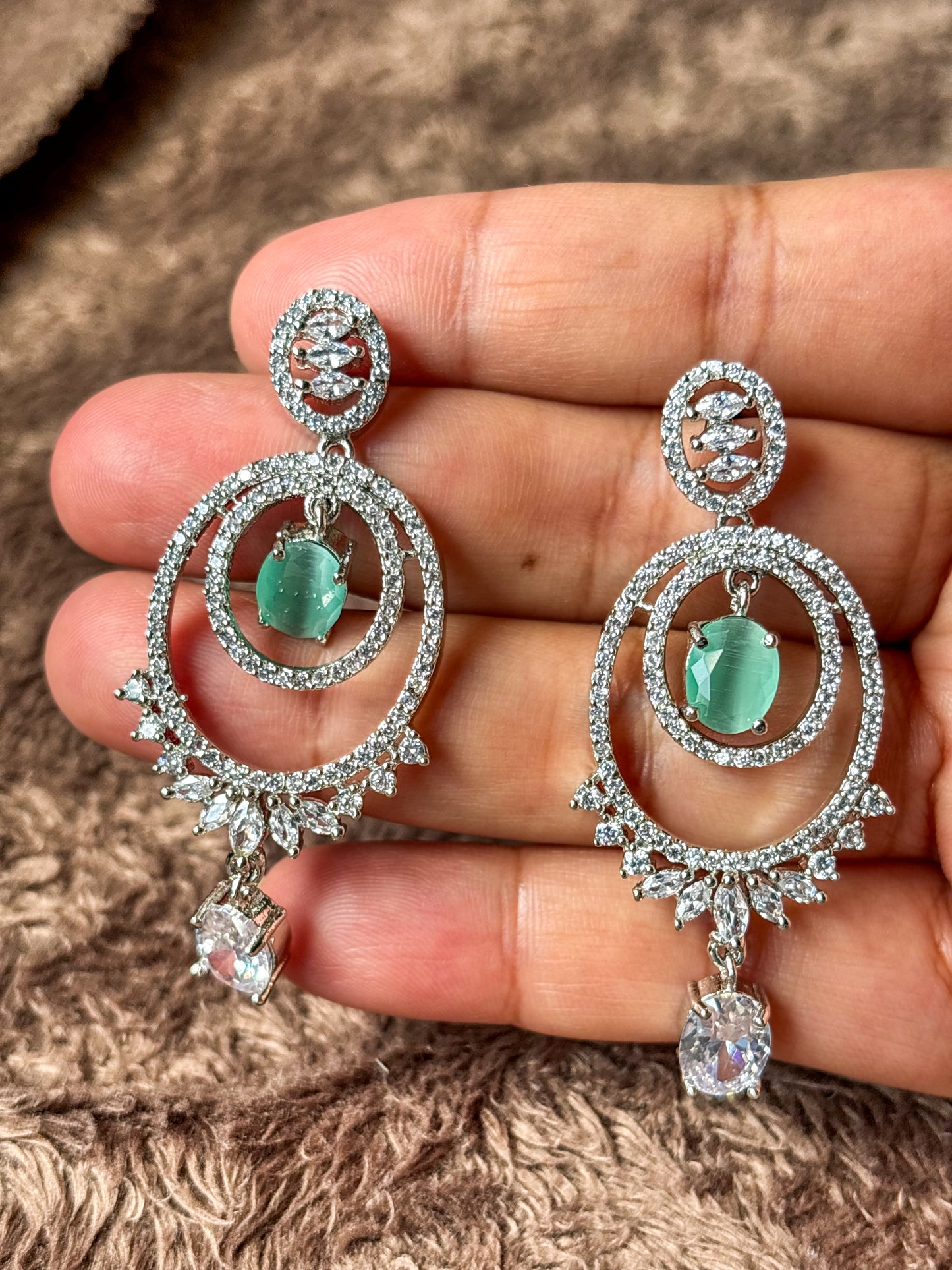 Elegant silver-tone chandelier earrings with emerald green center stones and sparkling zircon detailing.