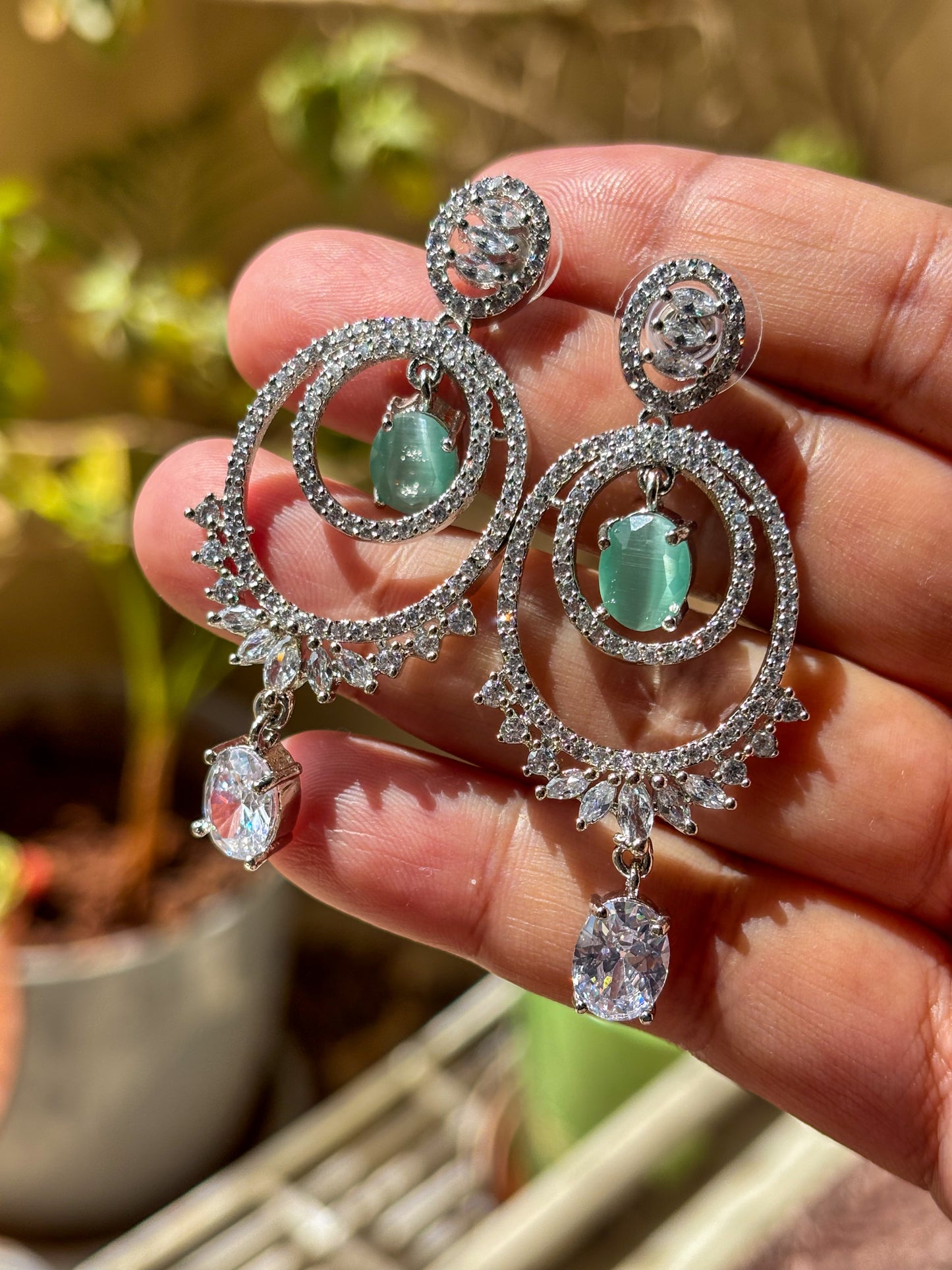 Elegant silver-tone chandelier earrings with emerald green center stones and sparkling zircon detailing.