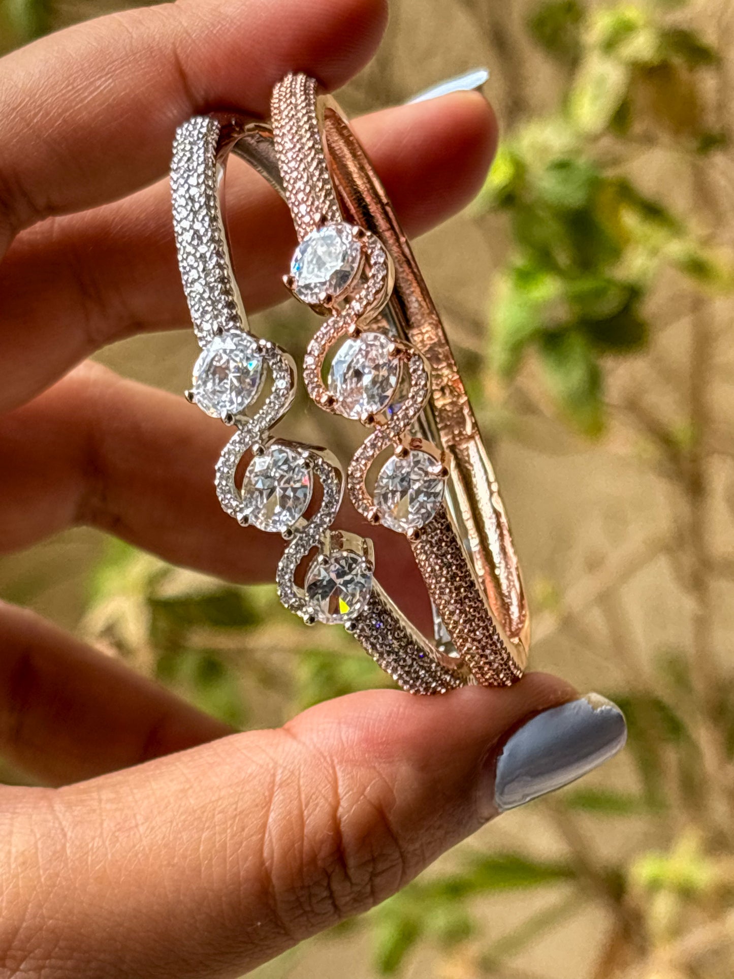 Elegant rose gold & silver AD bracelets with sparkling stones on a smooth wrist, photographed on a soft textured fabric background in warm natural lighting.