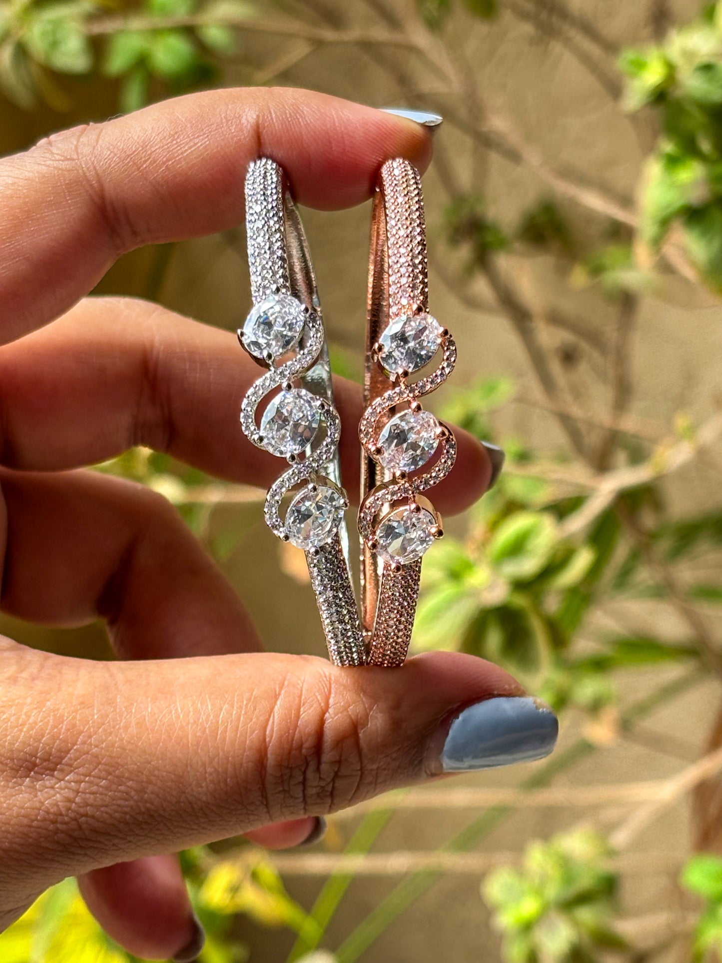 Elegant rose gold & silver AD bracelets with sparkling stones on a smooth wrist, photographed on a soft textured fabric background in warm natural lighting.