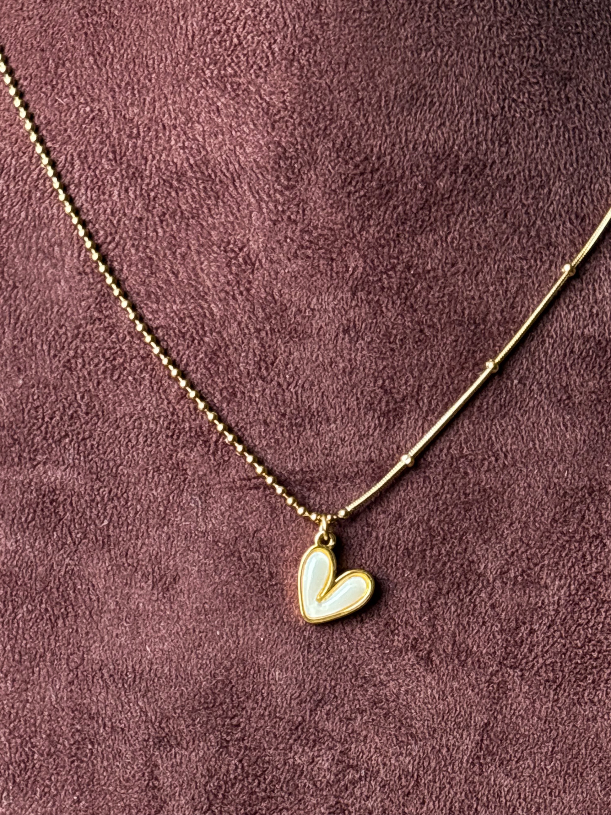 Gold-tone dual-chain necklace featuring a delicate ball chain and snake chain design with a white enamel heart pendant. Perfect minimalist jewellery for everyday wear.