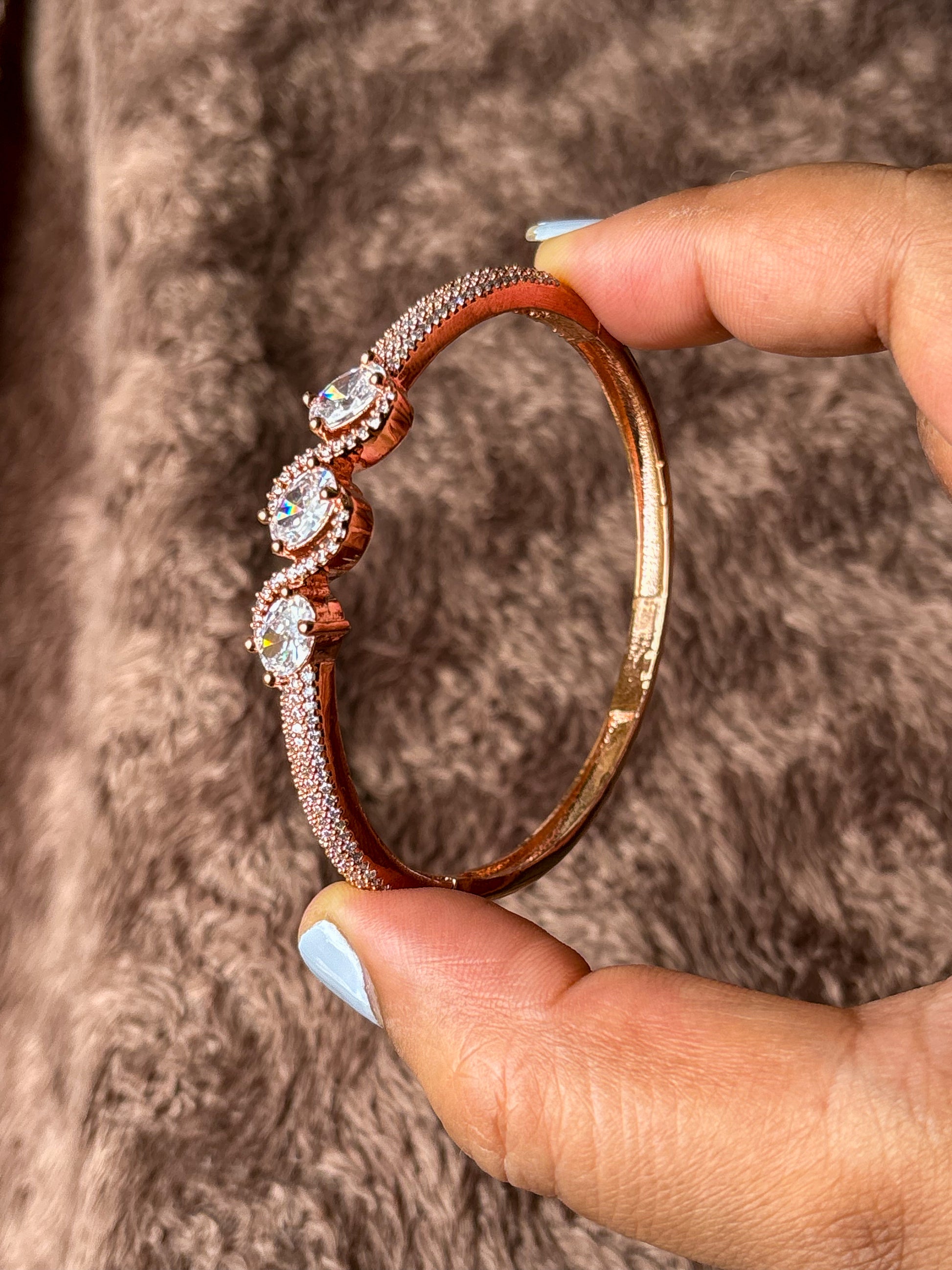 Elegant rose gold & silver AD bracelets with sparkling stones on a smooth wrist, photographed on a soft textured fabric background in warm natural lighting.