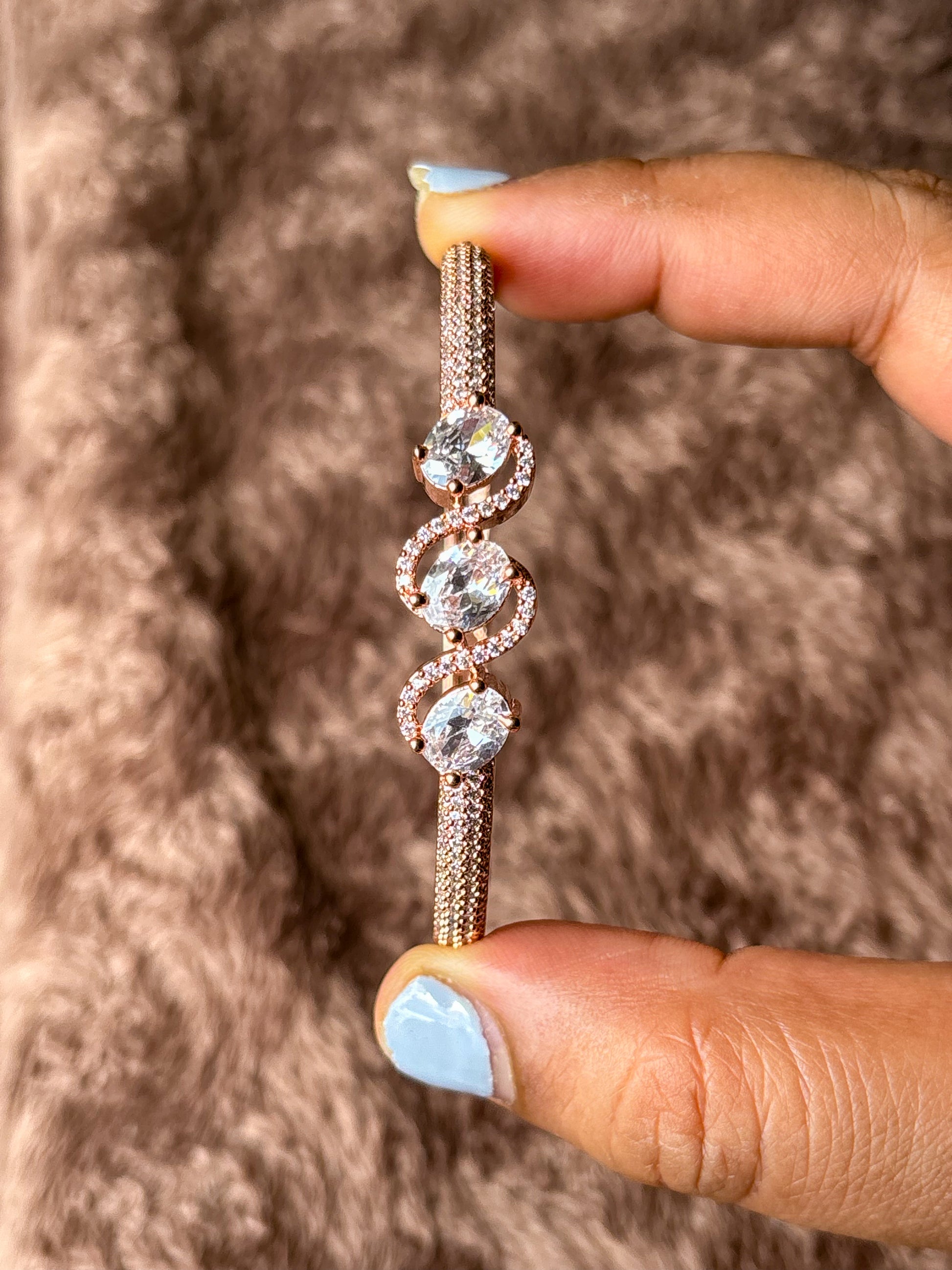 Elegant rose gold AD bracelet with sparkling stones on a smooth wrist, photographed on a soft textured fabric background in warm natural lighting.