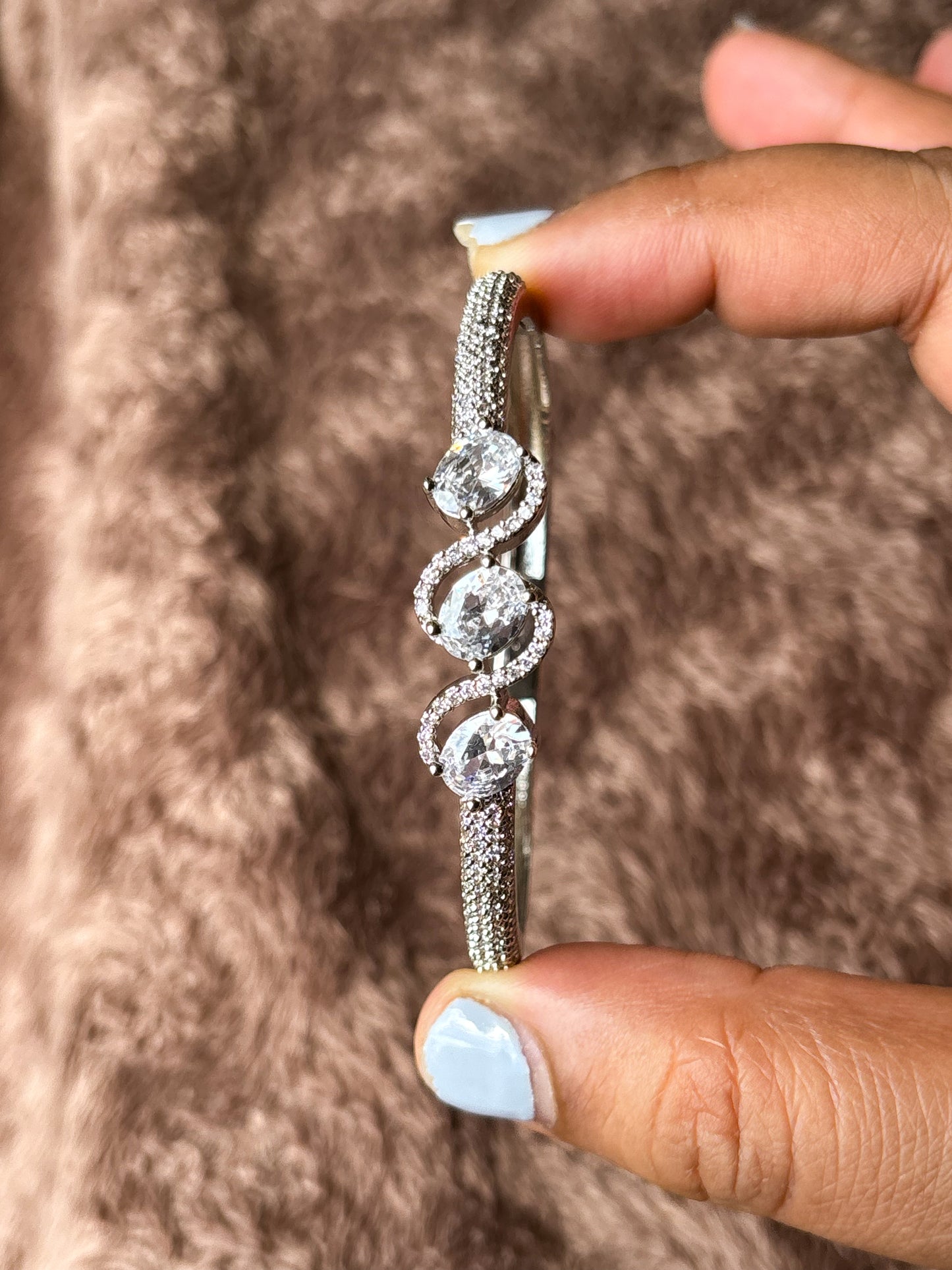 Elegant rose gold & silver AD bracelets with sparkling stones on a smooth wrist, photographed on a soft textured fabric background in warm natural lighting.