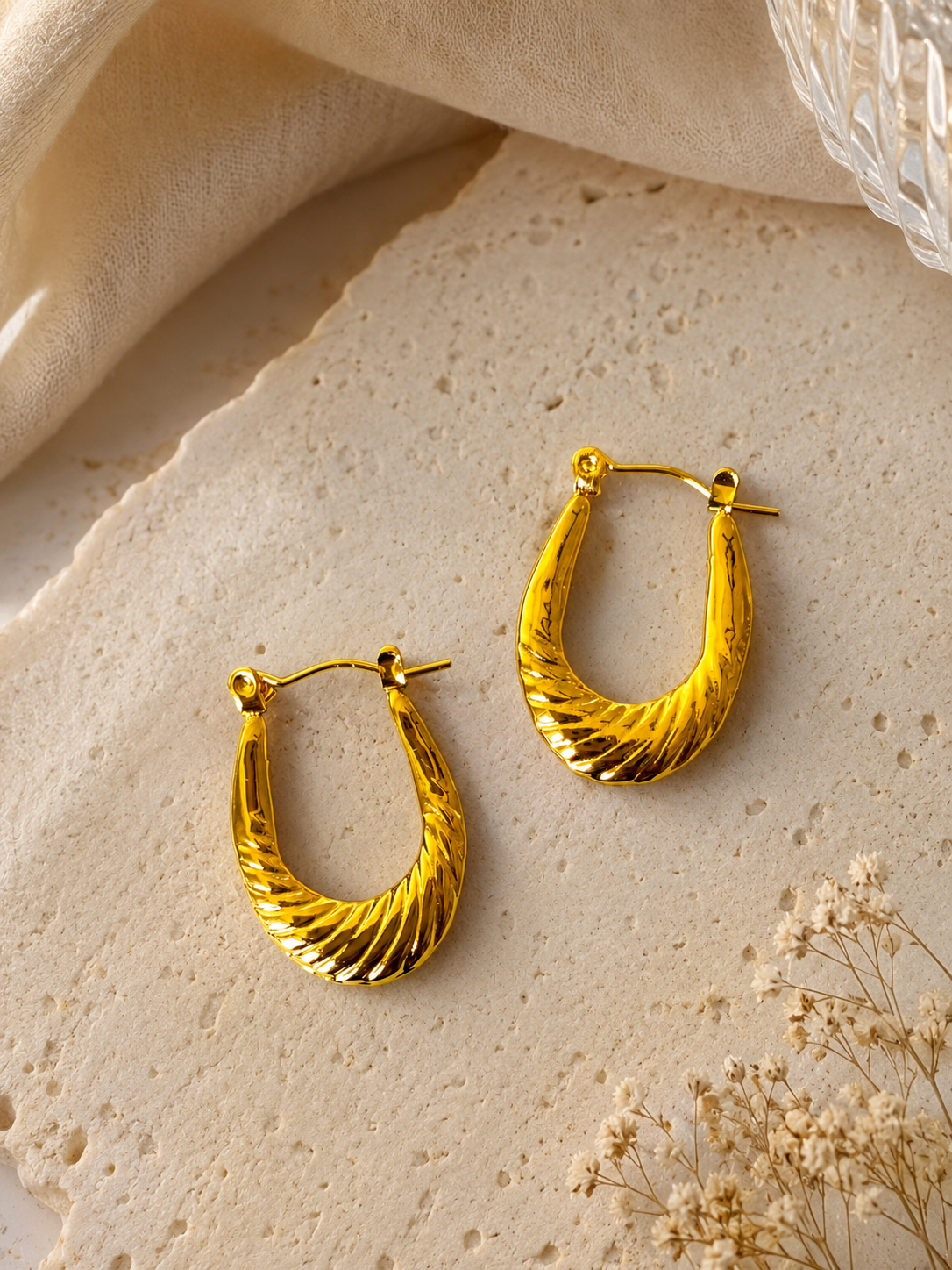 Anti tarnish textured gold hoop earrings with a sculpted twisted design, displayed on a soft neutral aesthetic background. Lightweight waterproof statement hoops with a polished gold finish for everyday wear.