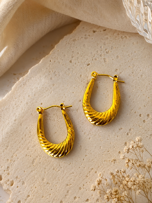 Anti tarnish textured gold hoop earrings with a sculpted twisted design, displayed on a soft neutral aesthetic background. Lightweight waterproof statement hoops with a polished gold finish for everyday wear.
