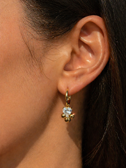 Close-up of an ear wearing a gold earring with a clear gemstone.
