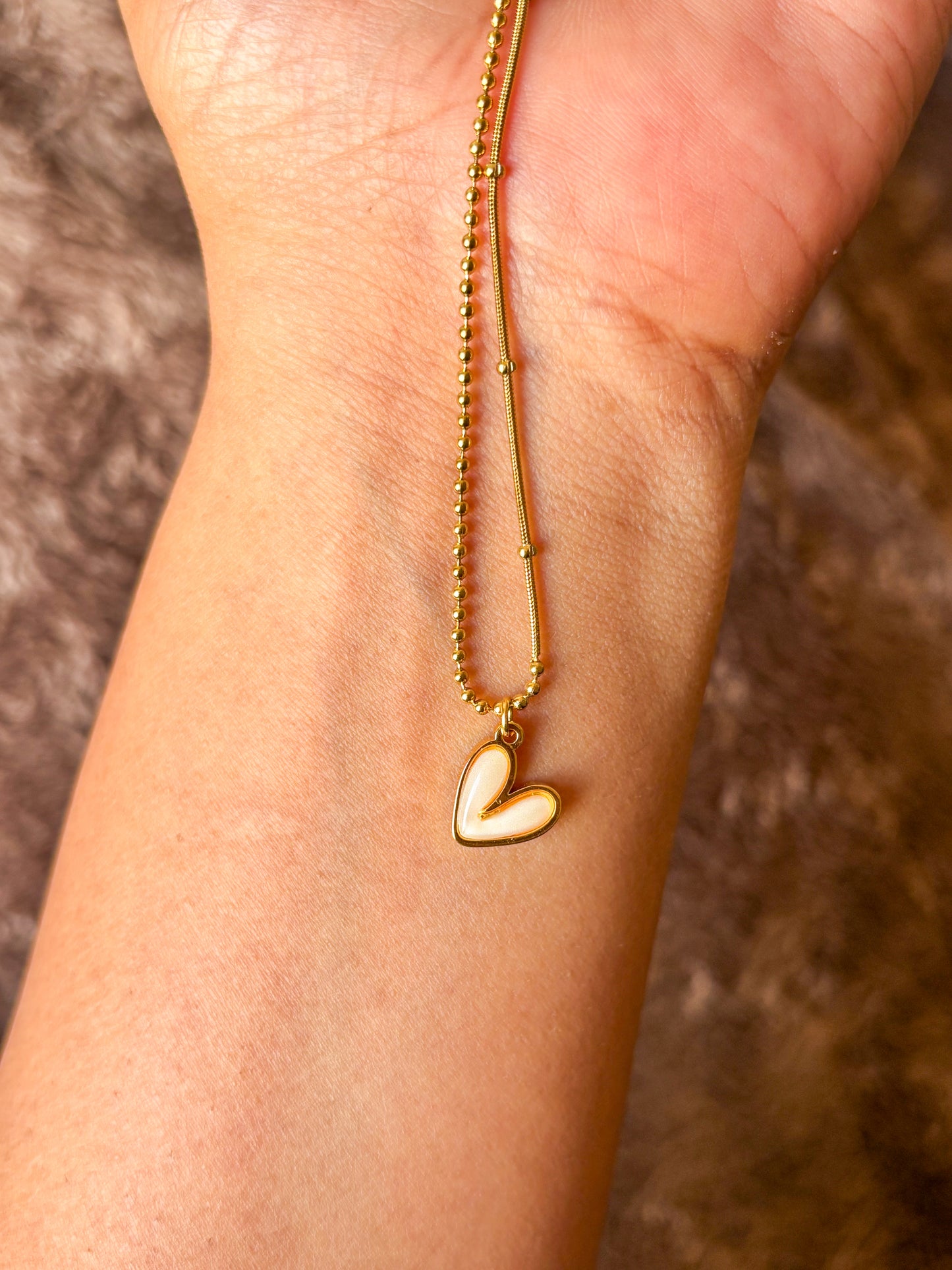 Gold-tone dual-chain necklace featuring a delicate ball chain and snake chain design with a white enamel heart pendant. Perfect minimalist jewellery for everyday wear.